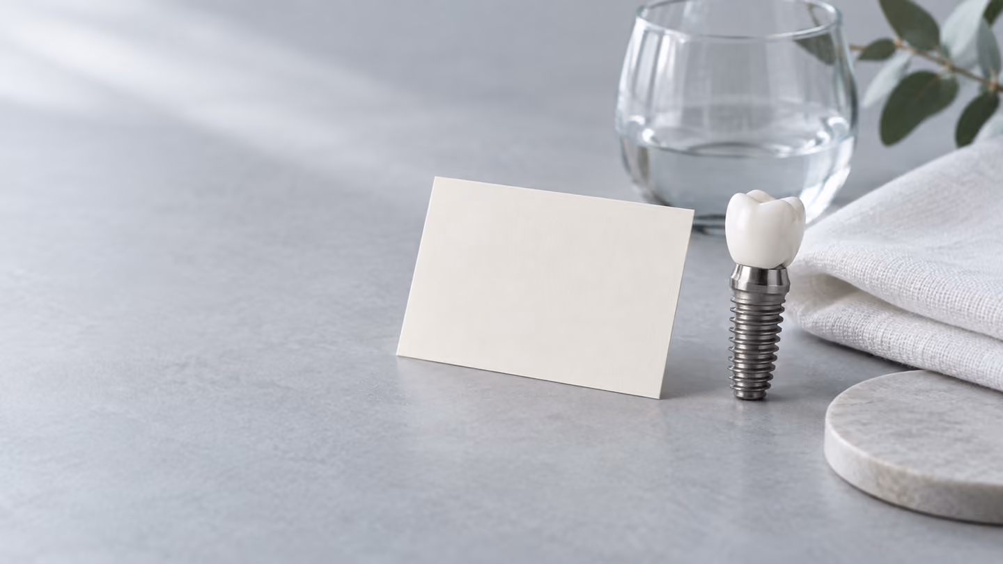 Illustrative still life of a dental implant model, blank card and glass on a table